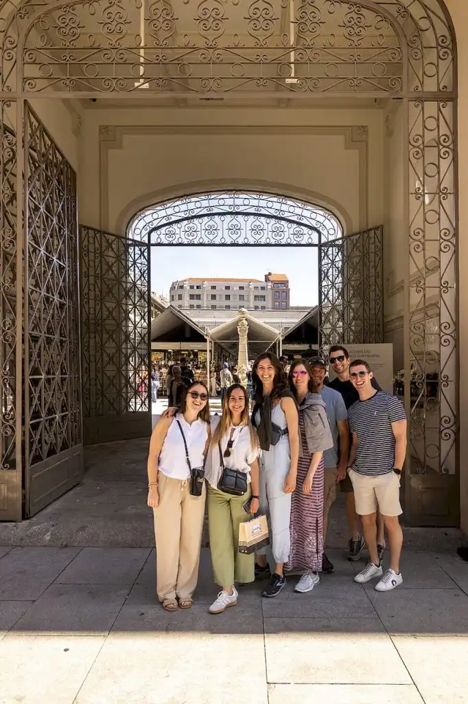 A group of seven guests posing at the ornate iron entrance gates of a Portuguese market