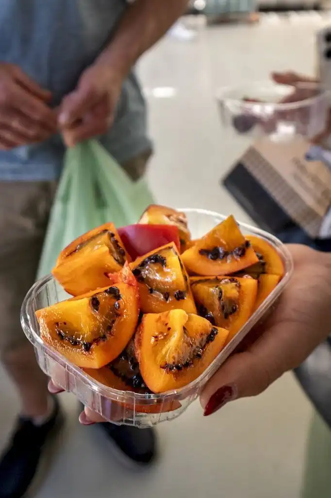 Sliced mango seasoned with dark spice in a clear plastic container, held in a hand