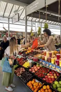 A vendor handing a bag of fruit to a customer at an indoor market stall