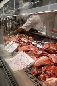 Raw pork cuts displayed in a butcher's refrigerated counter with handwritten price signs