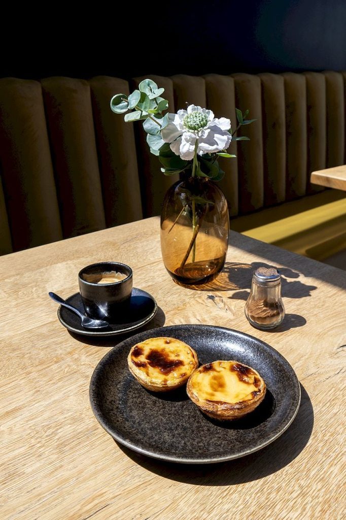 Two pastel de nata custard tarts on a dark ceramic plate beside an espresso