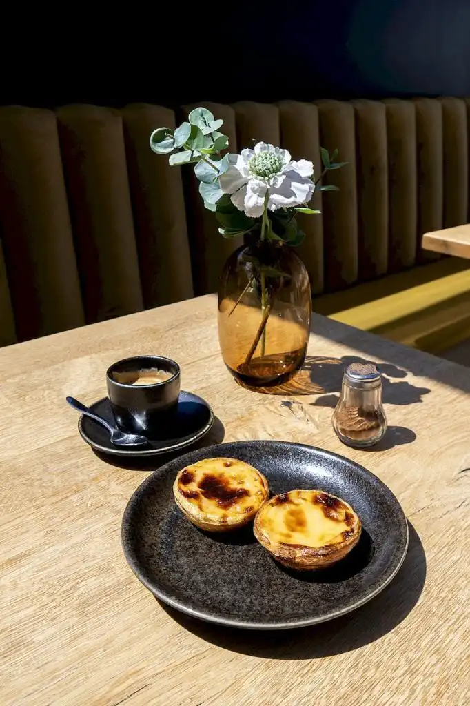 Two pastel de nata custard tarts on a dark ceramic plate beside an espresso