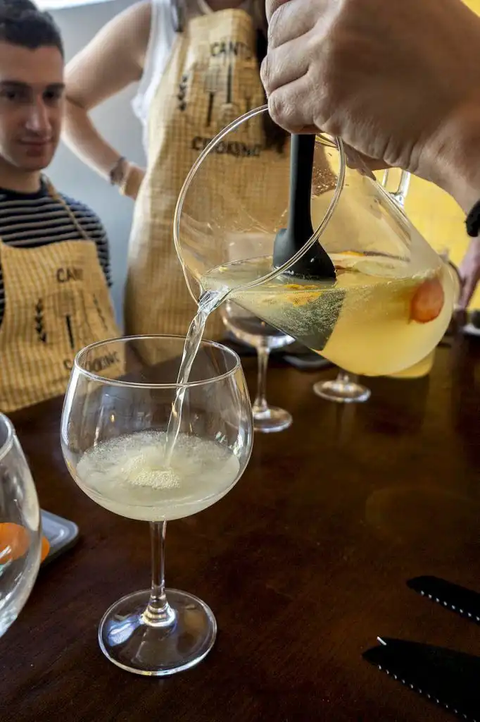 A light drink being poured from a pitcher into a large stemmed glass