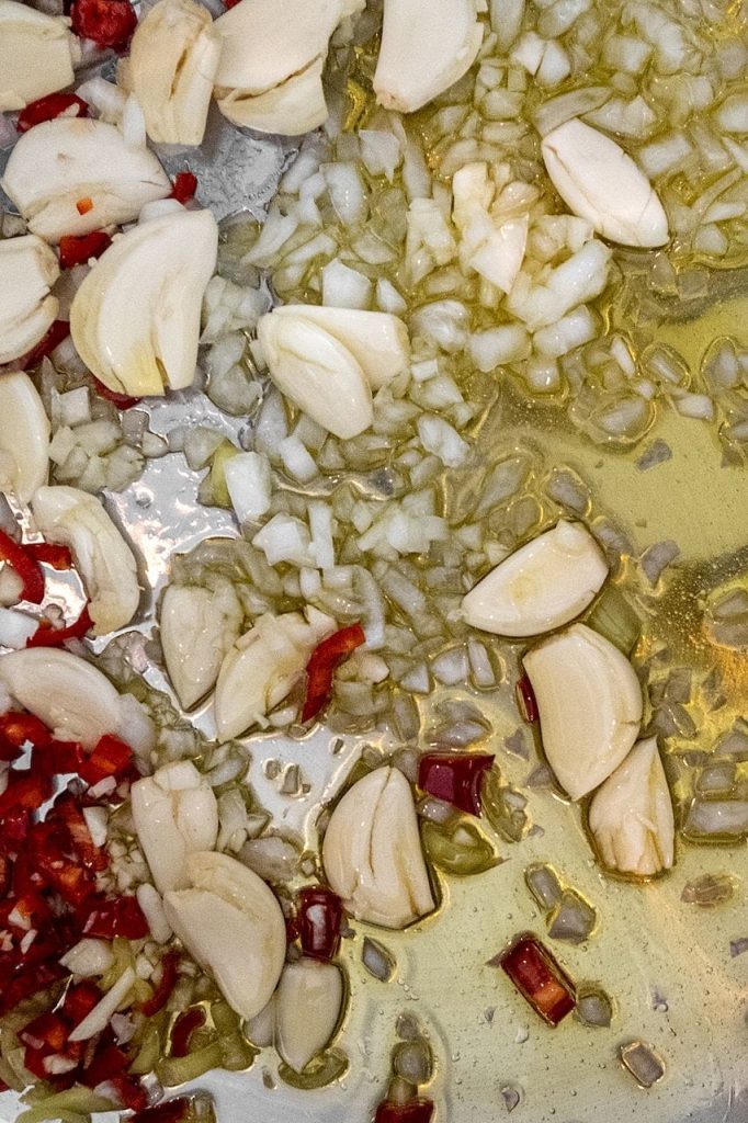 Sliced garlic cloves and chopped red chilli sautéing in olive oil in a wide pan