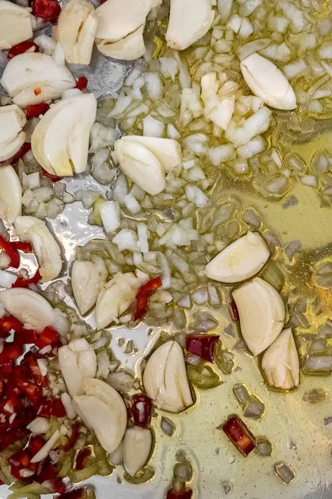 Sliced garlic cloves and chopped red chilli sautéing in olive oil in a wide pan