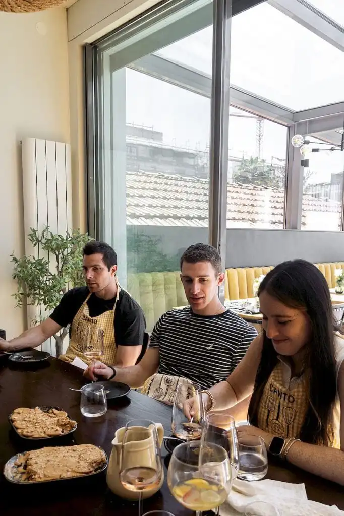 Three guests seated at a dining table wearing yellow gingham aprons, with food and wine glasses in front of them