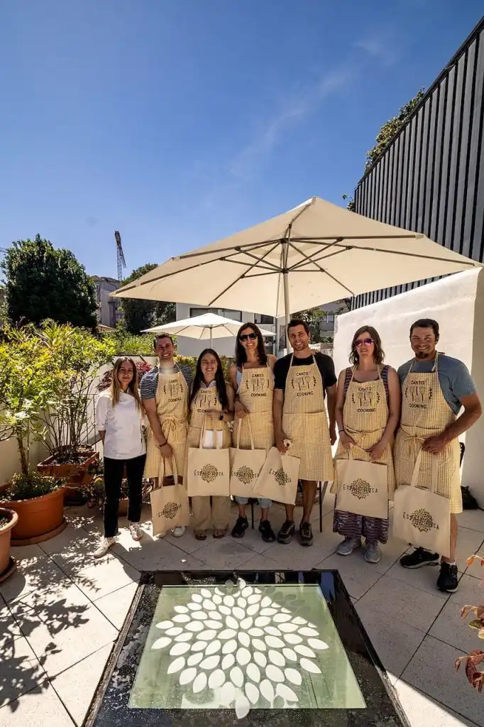 A group of guests and a chef wearing matching yellow gingham Canto Cooking aprons on a sunny rooftop terrace