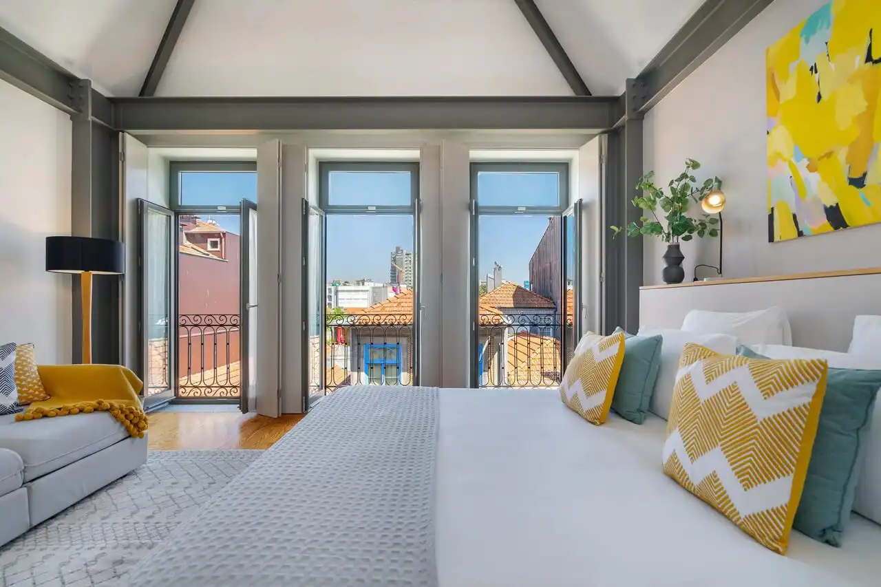 Bright bedroom at Canto de Luz with open French doors onto a wrought-iron balcony above Porto rooftops