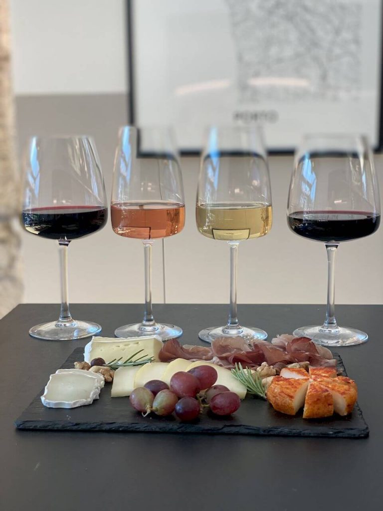 Four wine glasses with red, rosé, white, and red wines beside a charcuterie and cheese board