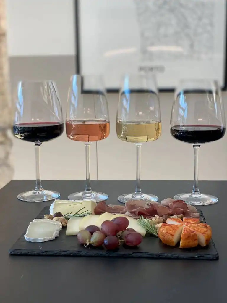 Four wine glasses with red, rosé, white, and red wines beside a charcuterie and cheese board