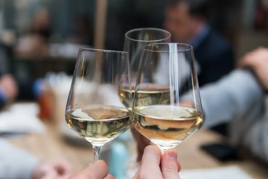 Two guests clinking glasses of white wine at a restaurant table
