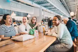Four guests laughing and smiling together at a counter inside a Portuguese food market