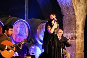 A singer performing fado with two guitarists in a wine cellar