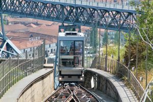 Funicular car ascending a hillside rail track beneath a large iron bridge in Porto