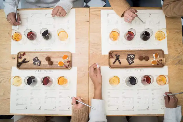 Overhead view of a wine tasting session with four place settings, tasting scorecards, and food pairings on wooden boards