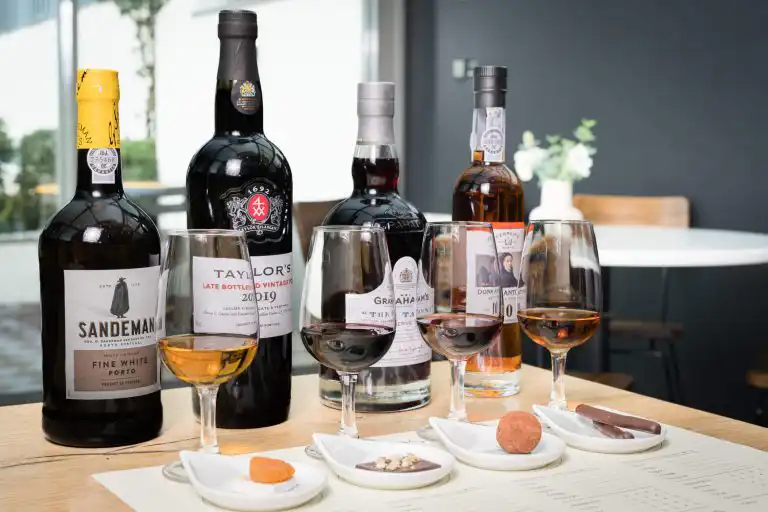 Four bottles of Port wine with tasting glasses and chocolate pairings on a wooden table
