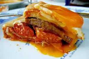 Francesinha sandwich smothered in orange beer and tomato sauce on a café plate