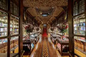 Interior of Livraria Lello bookshop in Porto, showing ornate carved wooden shelves, a sweeping red-carpeted staircase, and an elaborate ceiling