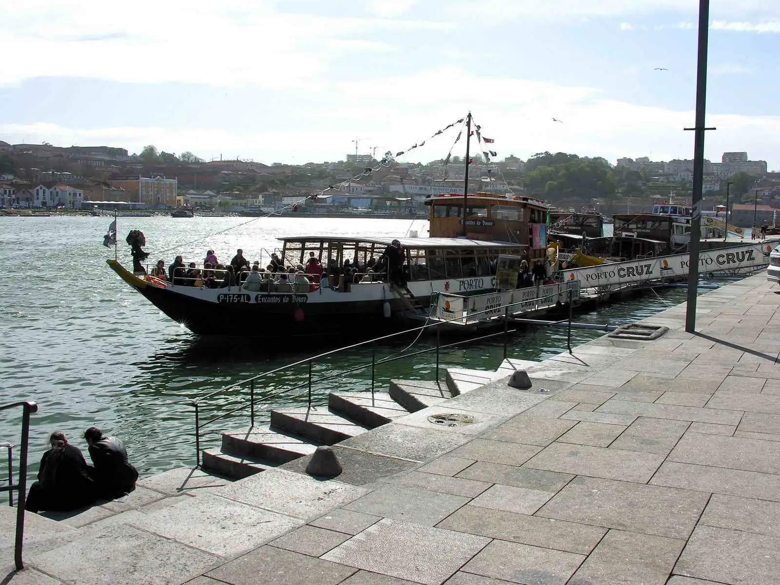 Tourist boat named Encantos do Douro docked at a Porto quay with a boarding ramp