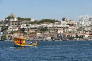 Vila Nova de Gaia waterfront viewed from the Douro River, with a yellow and blue tour boat in the foreground