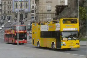 Yellow Bus and red hop-on hop-off sightseeing buses on a Porto city street